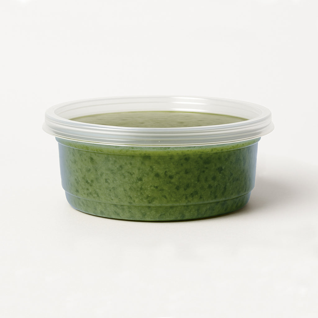Green basil pesto in a container with a lid on a white background