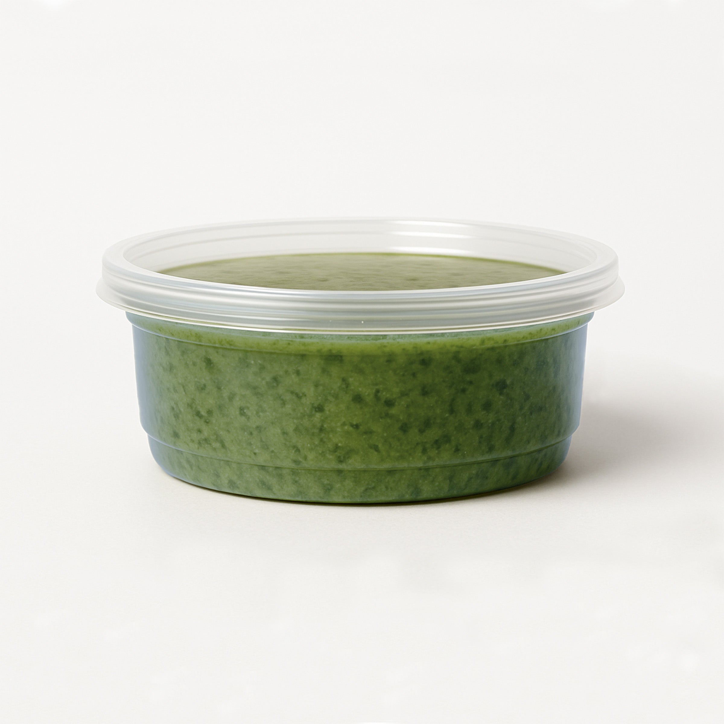 Green basil pesto in a container with a lid on a white background