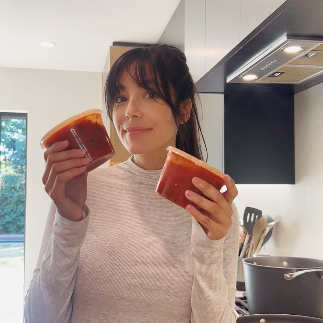 Woman holding two jars of red sauce in a kitchen